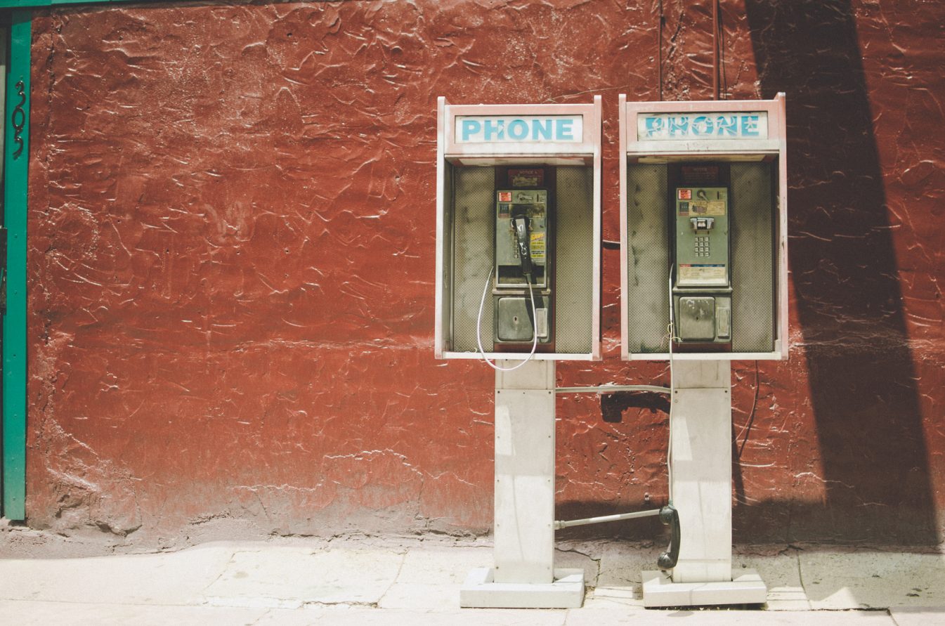 two old pay phones in front of a red brick wall